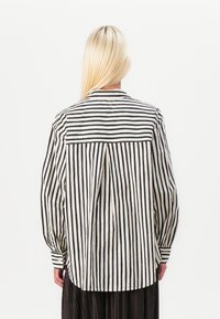 Maglietta a righe bianche e nere con polsini abbottonati, vestibilità leggermente ampia e design a yoke sul retro. Tessuto di una consistenza liscia.
