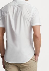 Camisa blanca de manga corta hecha de una tela suave, con un cuello clásico y un dobladillo curvado, con acentos en contraste en las mangas.