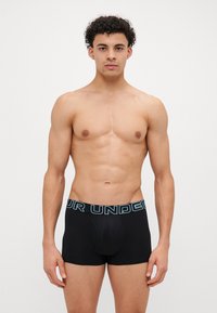Svarte boxershorts med en lyseblå "YOUR UNDER" midjebånddesign. Stoffet ser glatt og elastisk ut. Modellen vises frontvendt.