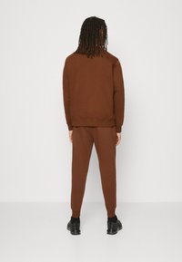 Brown cotton sweatshirt and pants set, featuring ribbed cuffs and a relaxed fit, paired with black sneakers. Simple design, no patterns.