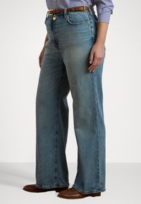 Svetlo modré džíny s širokými nohavicami vyrobené z denimu, s vysokým pásom a prednými vreckami, doplnené hnedým opaskom a hnedými slip-on topánkami.