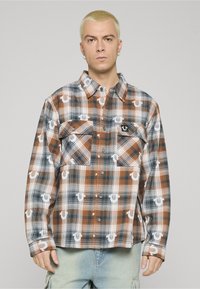 Camicia a quadri con bottoni in tonalità di marrone, blu e bianco, con due tasche sul petto e dettaglio con logo. Realizzata in tessuto leggero con vestibilità comoda.