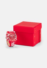Red Diesel watch with a round face, textured red dial, and silver hardware. Features a patterned red and white strap. Accompanied by a matching box.