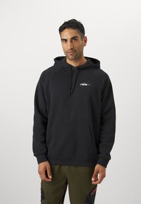 Haut à capuche noir en tissu doux avec une poche frontale et un cordon de serrage. Présente un petit design graphique sur la poitrine.