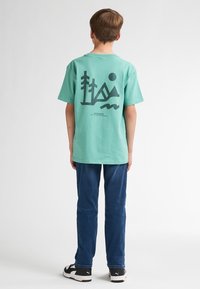 Tricou din bumbac turcoaz cu un grafic al muntelui negru pe spate, asortat cu blugi blue denim și pantofi sport negri.