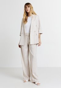 Ensemble composé d'un blazer rayé de couleur claire et d'un pantalon large, fabriqué à partir d'un tissu texturé. Présente un design à double boutonnage et une coupe décontractée.