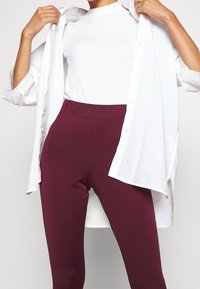 White button-up shirt over a form-fitting, ribbed white top and high-waisted, stretchy burgundy leggings, emphasizing texture and fit.
