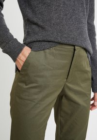 Un pull en tricot gris assorti à un pantalon vert olive avec des poches latérales et des détails de couture subtils.