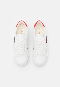 Vita snörskor med en röd hälflik, guldakcenter och blommig broderi på sidorna. Slät läderovandel och gummisula.