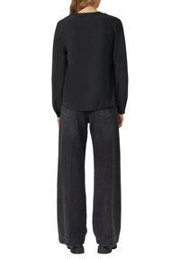 Schwarze Bluse mit langen Ärmeln und rundem Halsausschnitt, kombiniert mit locker sitzender dunkelgrauer Denim-Jeans. Weiche Textur und entspannte Silhouette.