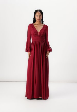 Robe longue bordeaux avec un décolleté en V profond, un corsage plissé et des manches longues. Le tissu fluide crée une silhouette drapée. Texture lisse.