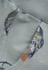 Kurzärmeliges Hemd aus hellblauem Stoff mit einem illustrierten Hundedesign in den Farben Grün, Beige und Braun, ergänzt durch strukturierte Akzente.