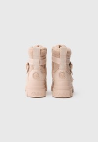 Par de botas beige de caña alta, forradas con borrego, con suelas gruesas y logotipos de la marca "Buffalo" en los talones y correas, mostradas desde atrás.