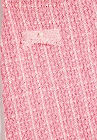 Rosa vævet stof med et struktureret mønster, der har en lille, frynsede lap og en perleknap som accent.