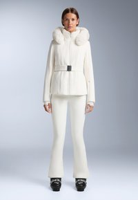 Fehér sídzseki, prémes kapucnival, strukturált dizájnnal, bordás textúrával, deréknál övvel szűkítve, fehér sínadrággal és fekete csizmával párosítva.