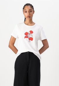 Witte t-shirt met een rood bloemmotief. Korte mouwen, ronde hals, gemaakt van zachte stof. Gecombineerd met zwarte broek.