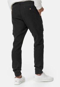 Pantalones cargo negros hechos de una tela suave, con bolsillos laterales, puños elásticos y un diseño ajustado. Combinados con zapatillas blancas.