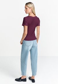 Kortsideline maroon top, millel on soonikuline tekstuur ja lainelised varrukad, koos helesiniste kõrge vöökohtadega kitsaste teksade ja mustade mokassiinidega.