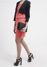 Korallklänning med avslappnad passform, kombinerad med en svart kort jacka. En svart kuvertväska och klackar med remmar i svart fulländar outfiten.