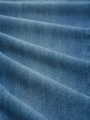 Tissu en denim avec une texture lisse ; couleur bleu moyen avec des variations subtiles. Présente un motif de tissage diagonal et un léger éclat dû à la finition du tissu.