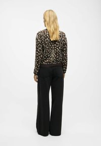 Knit sweater with a brown and cream spotted pattern, featuring a ribbed hem; paired with high-waisted, wide-leg black jeans.