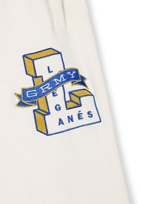 Biała tkanina z niebieskim i żółtym haftowanym wzorem. Zawiera litery w blokowym stylu z wstążkowym designem, mówiąc "GRMY" i "LEGANÉS."
