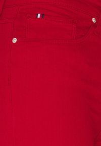 Jeans de mezclilla rojos con una textura suave, que cuentan con un pequeño bolsillo adornado con un patrón a rayas en azul, blanco y rojo. Detalle de remache plateado.