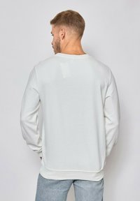 Sweatshirt blanc à manches longues avec une texture côtelée et un col rond. Doté d'un ourlet droit et d'une coupe décontractée. Design minimal.