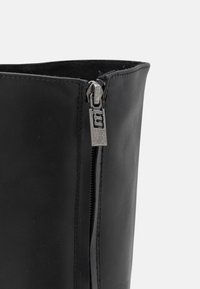 Bottes en cuir noir avec une fermeture éclair métallique, tirant en relief, extérieur lisse et forme structurée.