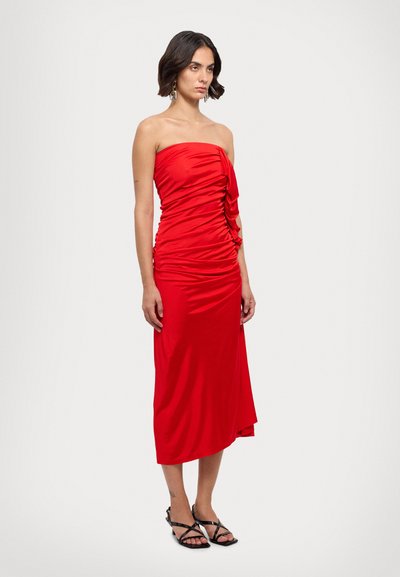 Κόκκινο strapless φόρεμα με ραμμένα πλαϊνά, μεσαίου μήκους, κατασκευασμένο από λείο ύφασμα. Διαθέτει μια κρεμαστή λεπτομέρεια στη μία πλευρά και ασύμμετρο στρίφωμα.