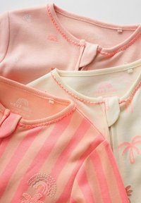 Trois body bébé pastel en rose, crème et pêche avec de petits motifs, des encolures festonnées et des fermetures éclair à l'avant.