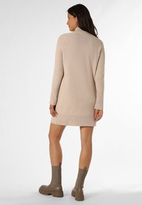 Beiges Strickkleid mit hohem Hals und langen Ärmeln, gerippten Bündchen und Saumdetail. Kombiniert mit braunen Stiefeletten mit einer dicken Sohle.
