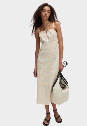 Kremowa sukienka midi z marszczonym wzorem i wiązaniem na szyi, w połączeniu z białą torbą z czarnymi akcentami oraz czarnymi sandałami na paski.