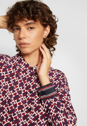 Camicia button-up con un motivo geometrico rosso e bianco, realizzata in tessuto morbido. I polsini presentano strisce a contrasto blu navy e bianche.