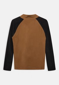 Långärmad topp med en brun kropp och svarta raglanärmar, tillverkad av ett slätt tyg med en subtil glans och hög krage.