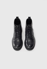 Bottines en cuir noir avec un bout arrondi, un laçage sur le devant et une semelle en caoutchouc. Texture lisse et design minimaliste avec une languette.