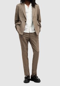 Kostkovaný oblek v odstínech béžové s sakem na jeden knoflík a odpovídajícími kalhotami. Bílé košile s krátkým rukávem a vzorem pod n ím. Černé boty s masivní podrážkou.