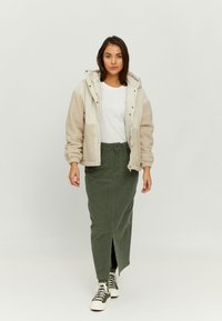 Beige and cream fleece-lined jacket with hood, paired with a green corduroy maxi skirt featuring a front slit, and white sneakers.