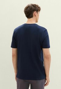 Námořnická modrá polo triko s krátkým rukávem z bavlny, s kulatým výstřihem a volným střihem. Zadní strana je hladká bez viditelného loga nebo vzorů.