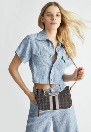 Chemise en denim bleu coupée avec un motif géométrique. Sac noir avec impression de logo et chaîne dorée, avec des rayures beiges et noires.