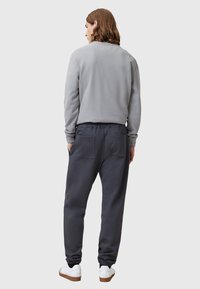 Grijze sweatshirt met ronde hals en lange mouwen, gecombineerd met donkergrijze joggingsbroek met elastische manchetten en achterzakken. Witte sneakers.