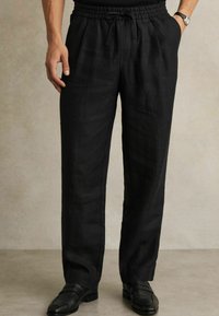 Fekete lenvászon nadrág, elasztikus derékpánttal és húzózsinórral, oldalsó zsebekkel és laza szabással, fekete elegáns cipőkkel párosítva.