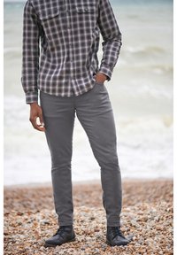 Camisa de franela a cuadros en negro y gris con dos bolsillos en el pecho, combinada con pantalones gris ajustados y botas negras de cordones.
