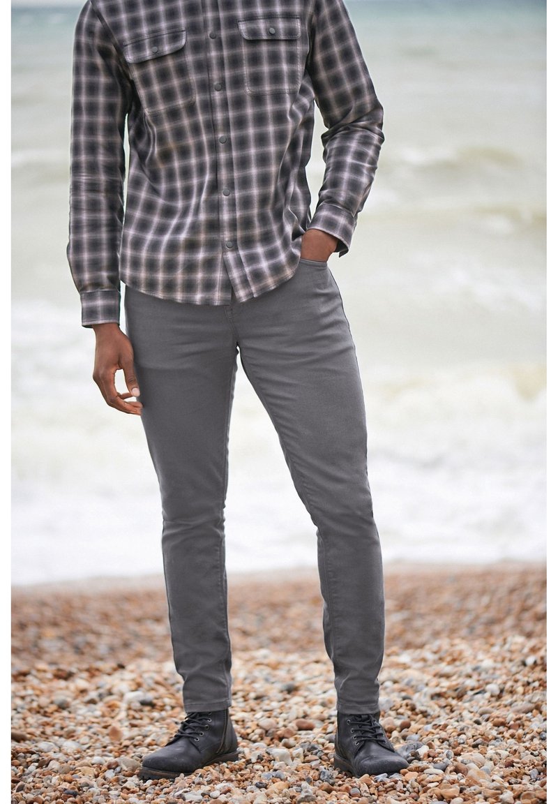 Camisa de franela a cuadros en negro y gris con dos bolsillos en el pecho, combinada con pantalones gris ajustados y botas negras de cordones.