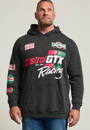 Homme portant un sweat à capuche noir Castrol GTX Racing avec logos et texte, debout bras détendus, sur un fond clair uni.