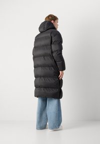 Sort quilted pufferjakke med et oversized design, der har en hætte, quiltet tekstur og en lang silhuet, parret med lyseblå viddebukser.