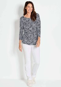 Langes Oberteil mit Navy- und weißen Paisleymuster, kombiniert mit weißen Hosen und weißen Sneakers. Es hat einen runden Ausschnitt und einen lässigen Schnitt.