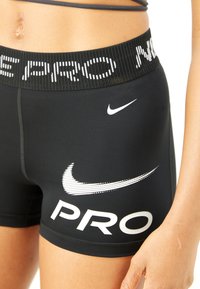 Primo piano di una persona che indossa pantaloni a compressione neri Nike Pro con loghi e testo bianchi sulla vita e sulla coscia.
