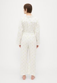 White pajama set with a textured, patterned fabric featuring yellow dots. Long sleeves, loose fit, and wide-legged trousers.