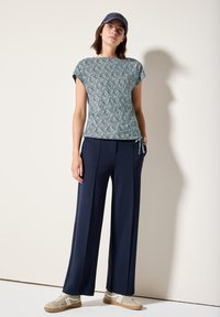 Krátký rukáv, vzorovaný top v modré a bílé barvě, spárovaný s námořnicky modrými kalhotami s širokými nohavicemi a béžovými teniskami. Měkká tkanina s uvolněným střihem.